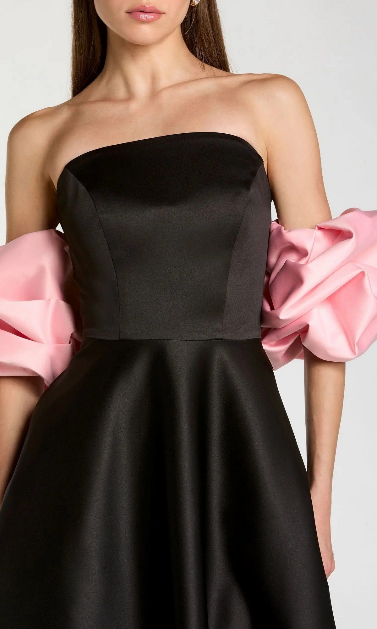 A woman wearing the Mac Duggal 21241 long formal dress—a striking black strapless satin gown featuring a fitted bodice and dramatic voluminous pink off-the-shoulder sleeves—photographed from the waist up.